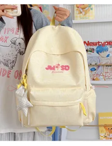 Detalle de mochila escolar de lona amarillo claro con letras bordadas y colgante de estrella.