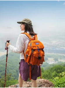 Oranger Outdoor-Reiserucksack Detailansicht mit mehreren Taschen, Karabiner und Wanderszene.