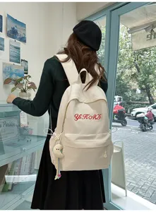 Detailansicht des cremefarbenen Canvas-Rucksacks mit roter Stickerei und Anhänger für Schule.
