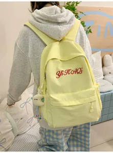 Gelber Canvas Schulrucksack mit gestickten roten Buchstaben und süßem Anhänger, Detailansicht.