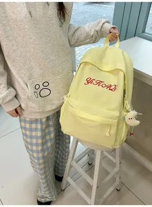 Detailansicht des gelben Rucksacks mit roter Buchstabenstickerei und süßem Plüschtier-Anhänger.
