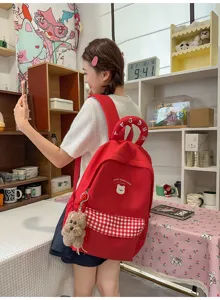 Detailansicht des roten Schülerrucksacks mit Karotasche, Bärenaufnäher und Plüschtier-Anhänger.