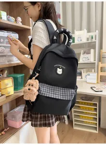 Detailansicht des schwarzen Schülerrucksacks mit Karomuster, Bärchen-Patch und Plüschhundeanhänger.