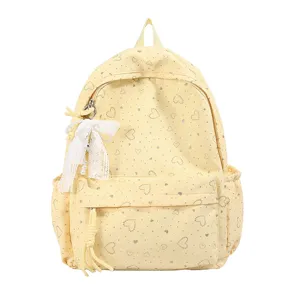 Gros plan du sac à dos scolaire jaune avec motif de cœurs et charmant nœud en dentelle.