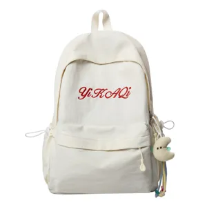 Detailansicht des lässigen weißen Canvas-Schulrucksacks mit roter Stickerei und Anhänger.