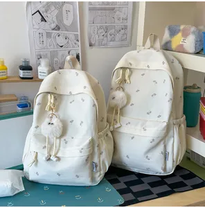 Detailansicht des niedlichen beige Studentenrucksacks mit Blumenmuster und flauschigem Anhänger.