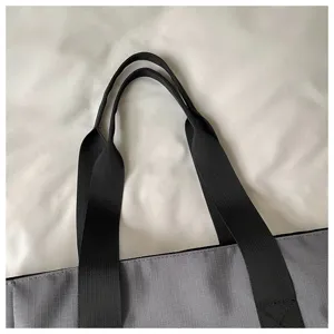 Primo piano dei manici della borsa tote in tela grigia con resistenti cinghie nere.
