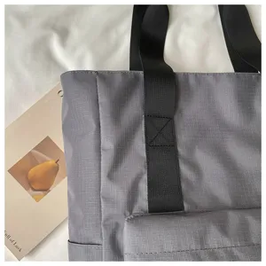 Borsa shopper grigia minimalista di grande capacità con manici neri e tasca frontale.
