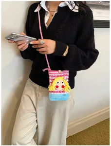 Nahaufnahme einer niedlichen gehäkelten Handytasche mit Puppen-Design in einer stylischen Alltagsszene.