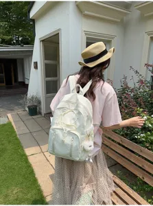 Detail view of white casual student backpack with drawstring and cute fluffy keychain outdoors.