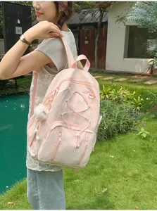 Detail view of pink student backpack with elastic cord and cute fluffy pendant outdoors.