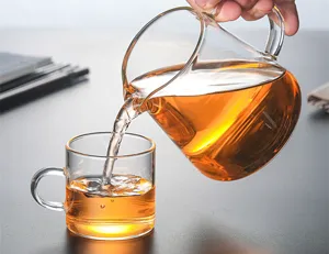 Gros plan détaillé d'une verseuse à thé en verre résistant, versant du thé dans une tasse.