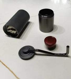 Parti smontate di macinacaffè manuale con macina in acciaio inossidabile e manico.