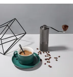 Detailansicht der manuellen Kaffeemühle mit Metallgehäuse und Keramiktasse Szene.
