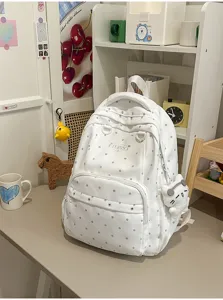 Vue détaillée du sac à dos blanc à pois avec pendentif en peluche et broderie frontale.