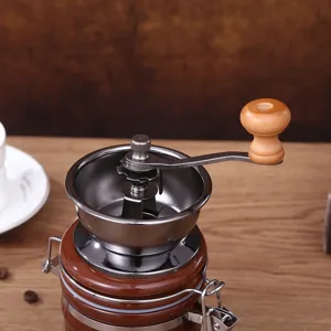Close-up detail of manual coffee grinder with ceramic jar and wooden handle crank knob.