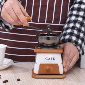 Detailansicht einer manuellen Vintage-Kaffeemühle mit Keramikkörper, Holzsockel und Metallgriff.