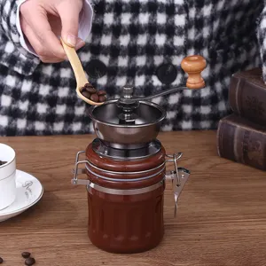 Portable manual coffee grinder with ceramic jar and wooden handle for fresh coffee beans at home.