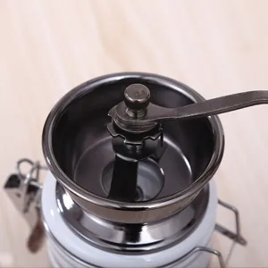 Vue détaillée d'un moulin à café manuel avec pot en céramique et manivelle en métal.