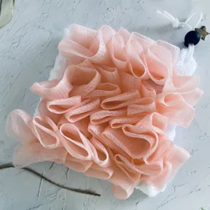 Detailopname van een zachte roze doucheploef gecombineerd met een wit zeepzakje.