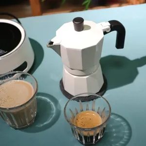 Detail view of white moka pot on table with coffee cups, perfect for home espresso brewing.