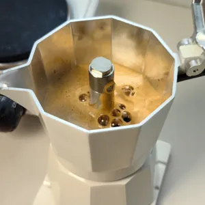 Detailed close-up shot of a white moka pot brewing fresh espresso coffee on stove.