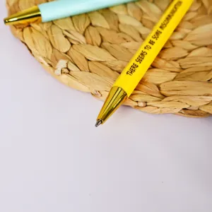 Nahaufnahme Detail eines Bueroklammer Kugel Schreibers mit goldener Spitze und witzigem Text.