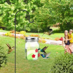 Detail view of a glass mason jar hummingbird feeder with red flower ports hanging in garden