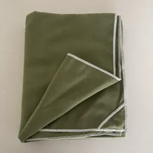 Vista detallada de una toalla verde doblada con costura blanca, textura de tela suave.