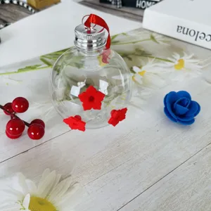 Detalle del comedero de colibríes de vidrio transparente con flores rojas y cinta.