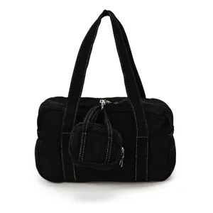 Black canvas tote bag detail view, contrasting white stitching, mini pouch pendant.