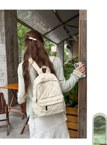 Quilted backpack detail showing soft cream fabric, neat stitching and front zip pocket.