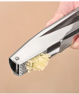 Close-up detail of stainless steel garlic press showing fresh garlic paste being squeezed.