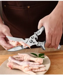 Detail view of heavy-duty stainless steel kitchen scissors cutting chicken bone in home kitchen.