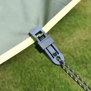 Gedetailleerde close-up van een zwarte plastic tentclip die een groen zeil vastzet.