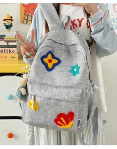 Gedetailleerd overzicht van grijze nylon schoolrugzak met kleurrijke geborduurde bloemen.