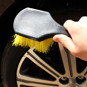 Detail view of a durable car tire brush with yellow bristles cleaning a vehicle wheel.