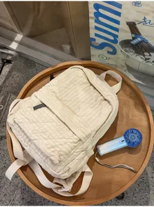 Detailed shot of a beige quilted plaid backpack on a wooden table, casual campus commuter style.