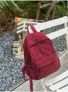 Detailed view of dark red plaid quilted backpack in outdoor natural scenic background.