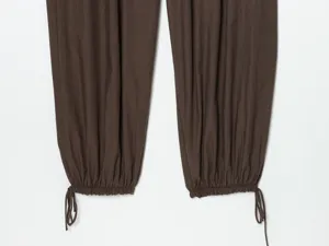 Dettaglio di pantaloni marroni da donna con coulisse regolabile e polsini arricciati.