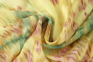 Close-up detail of smooth fabric with abstract floral print in vibrant yellow and green tones.