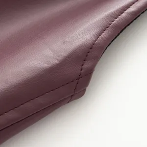 Close-up detail of burgundy faux leather garment texture with exquisite stitching work.