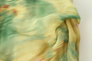 Close up view of lightweight draped fabric with artistic green and yellow watercolor print.