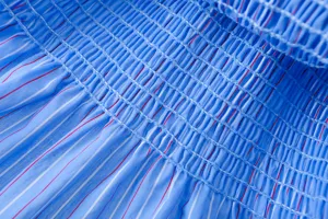 Blau und rot gestreifter Stoffdetail mit elastischem Waben-Smok-Strukturdesign.