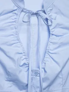 Primo piano della camicetta in popeline azzurro chiaro con lacci, arricciature e dettaglio bottone.