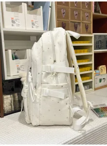 Detaillierte Seitenansicht eines weißen Schulrucksacks mit silbernen Sternen und Riemen.