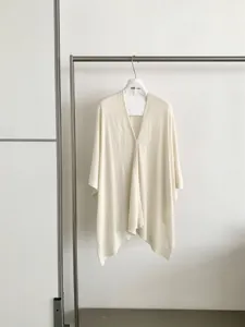 Dettaglio mantella in maglia beige, cardigan ampio casual, tessuto drappeggiato morbido.