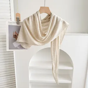 Vista detallada de chal de lino beige minimalista colgado en percha de madera clara.