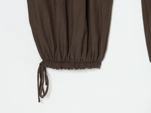 Vista dettagliata dell'orlo dei pantaloni marrone scuro con polsino elastico e coulisse regolabile.