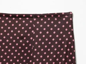 Close-up detail of brown fabric with pink polka dots, showing fine stitching and waistband.